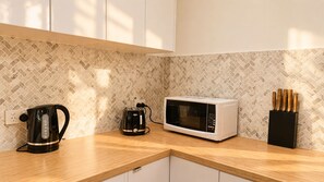 Une cuisine équipée d’un four à micro-ondes, d’une bouilloire et d’un bloc à couteaux, le tout posé sur un plan de travail en bois.