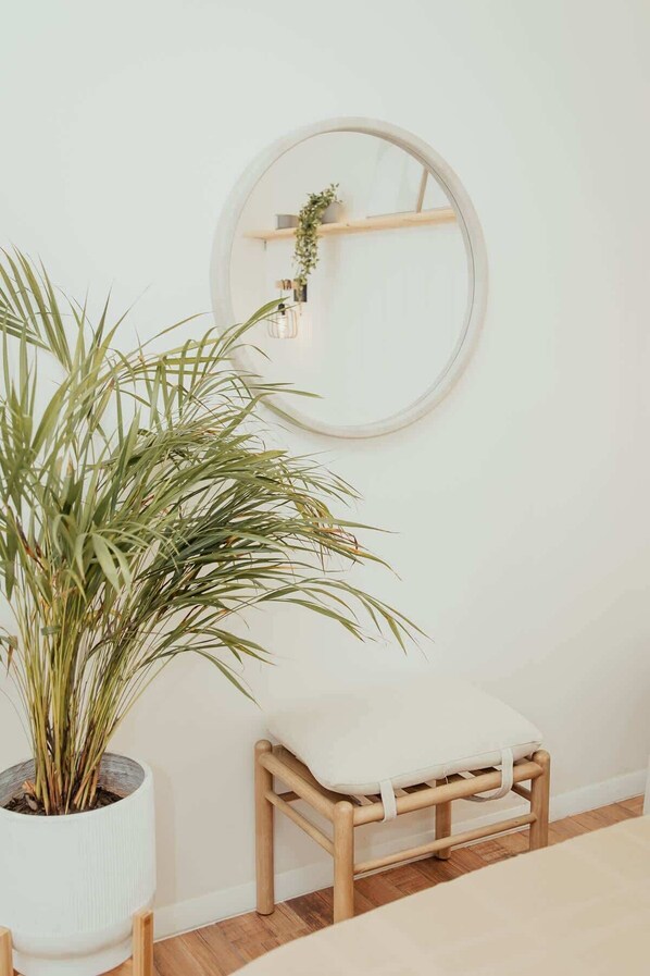 A minimalist room with a wooden stool, a potted plant, and a round mirror on the wall.