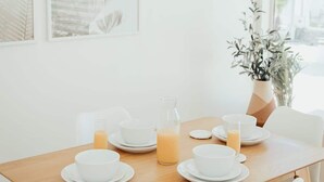 A dining area with a wooden table set for breakfast, white chairs, and a hanging light fixture. - Blvd Sunset. . . Beachfront Condos (Ensenada)
