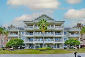 A multi-story hotel with balconies, a central courtyard, and palm trees. - First Floor Condo with Golf Course Views, Kids Bedroom and Near Attractions (Kissimmee)