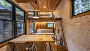 A cabin interior with a wooden interior, bunk beds, a dining table with chairs, and large windows. - Moving Inn Tokachi Kitanomori (Taiki)