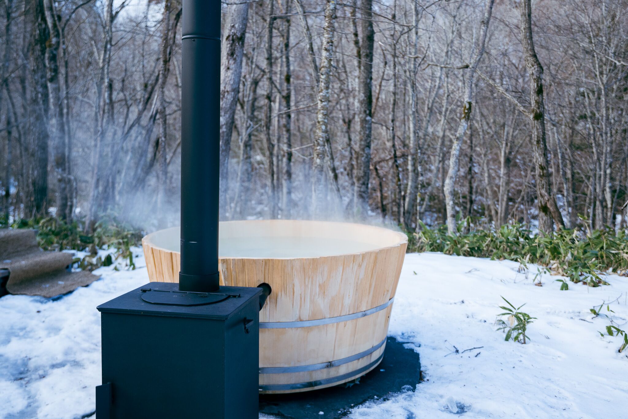 A wooden hot tub with a black heater in a snowy outdoor setting.