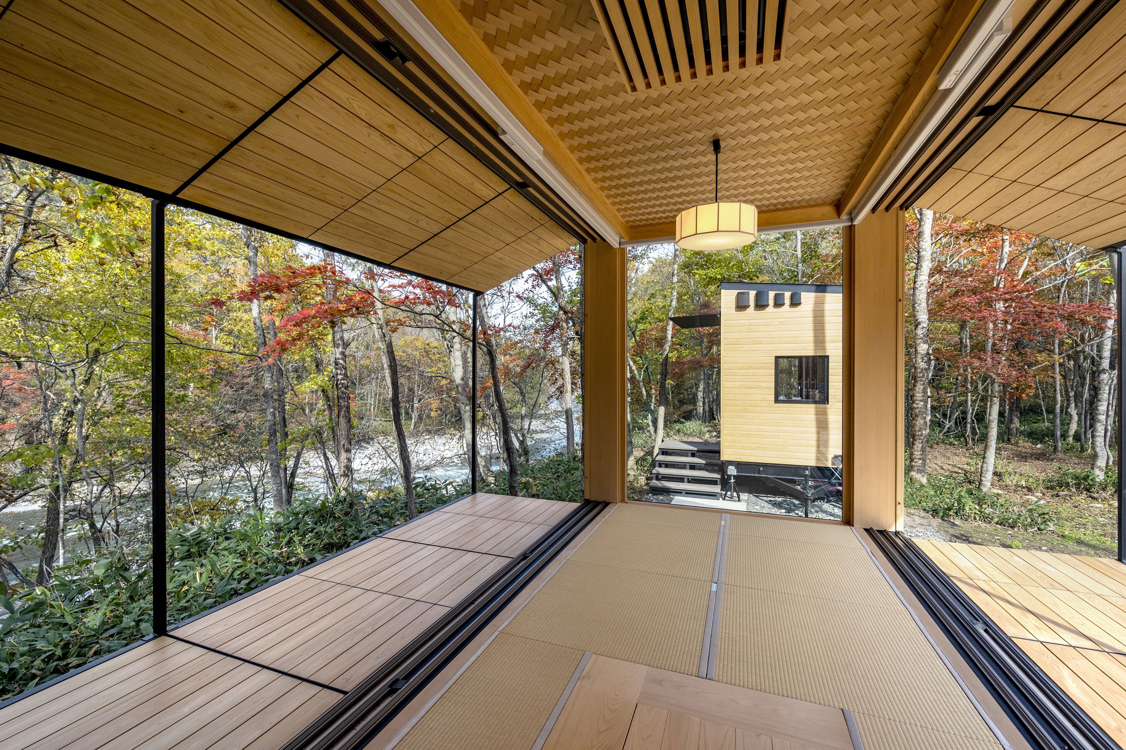 Un intérieur moderne avec de grandes fenêtres, un plancher en bois et une vue sur les arbres aux couleurs automnales.