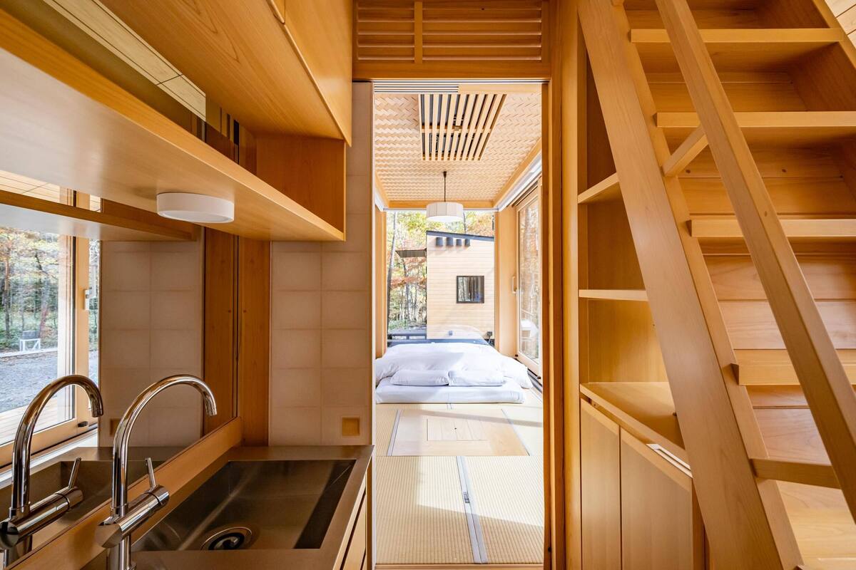 A modern interior with a wooden staircase, a kitchen area with a sink, and a bed with white linens.