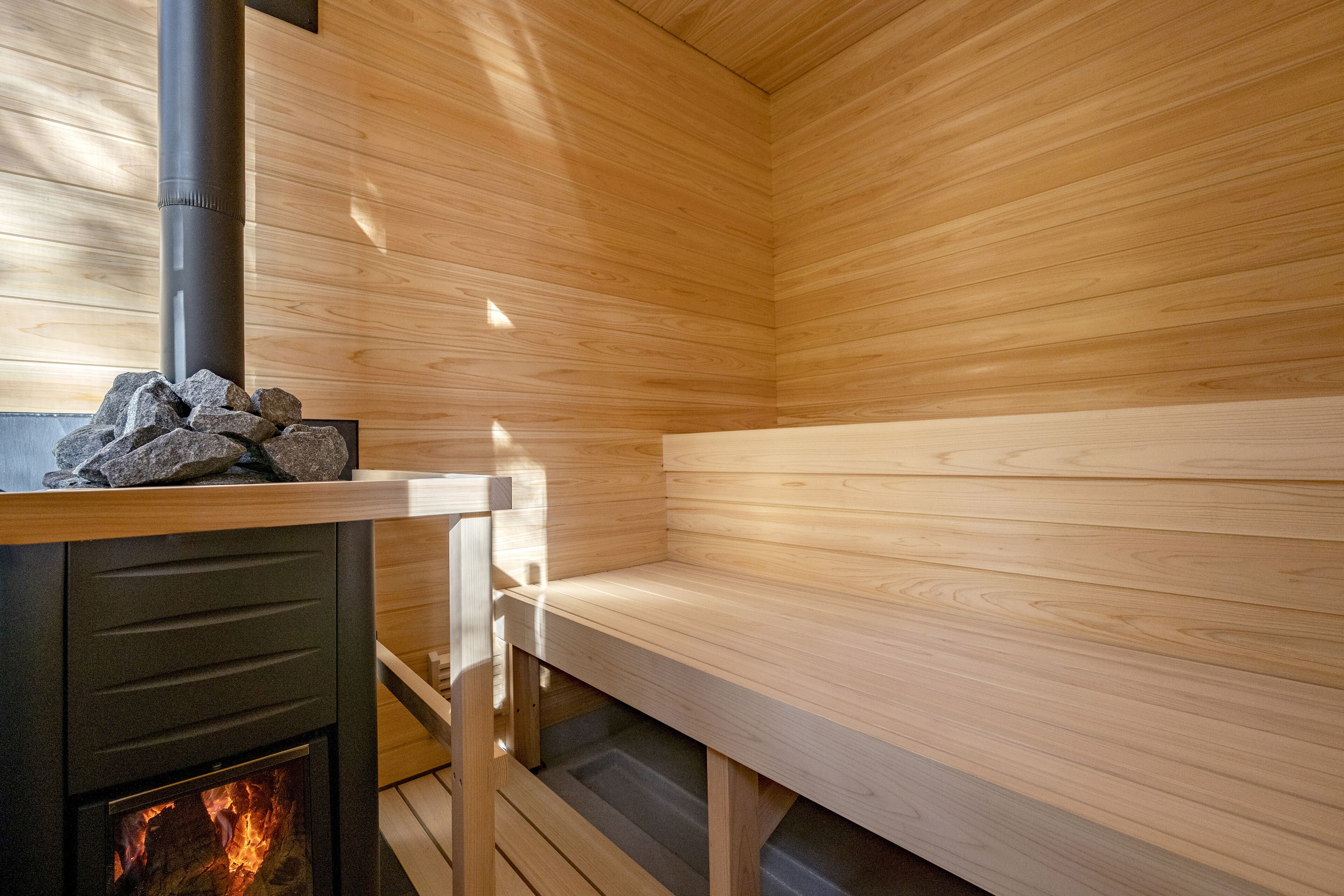 A sauna with wooden walls and benches, a visible fire, and a stone structure on the bench.