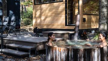 Een houten chalet met een hottub ervoor, omringd door bomen.