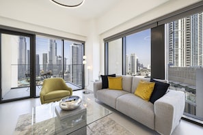 A modern living room with a sofa, a coffee table, and a chair, large windows with a city view, and a balcony. - 2BR | 2 Pools & Gym | Burj Khalifa | Dubai Mall (Dubai)