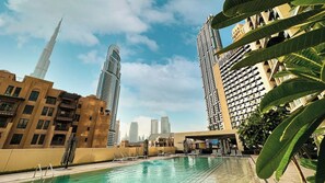 Une piscine entourée de chaises longues, bordée d’immeubles de grande hauteur et surplombant un ciel dégagé.