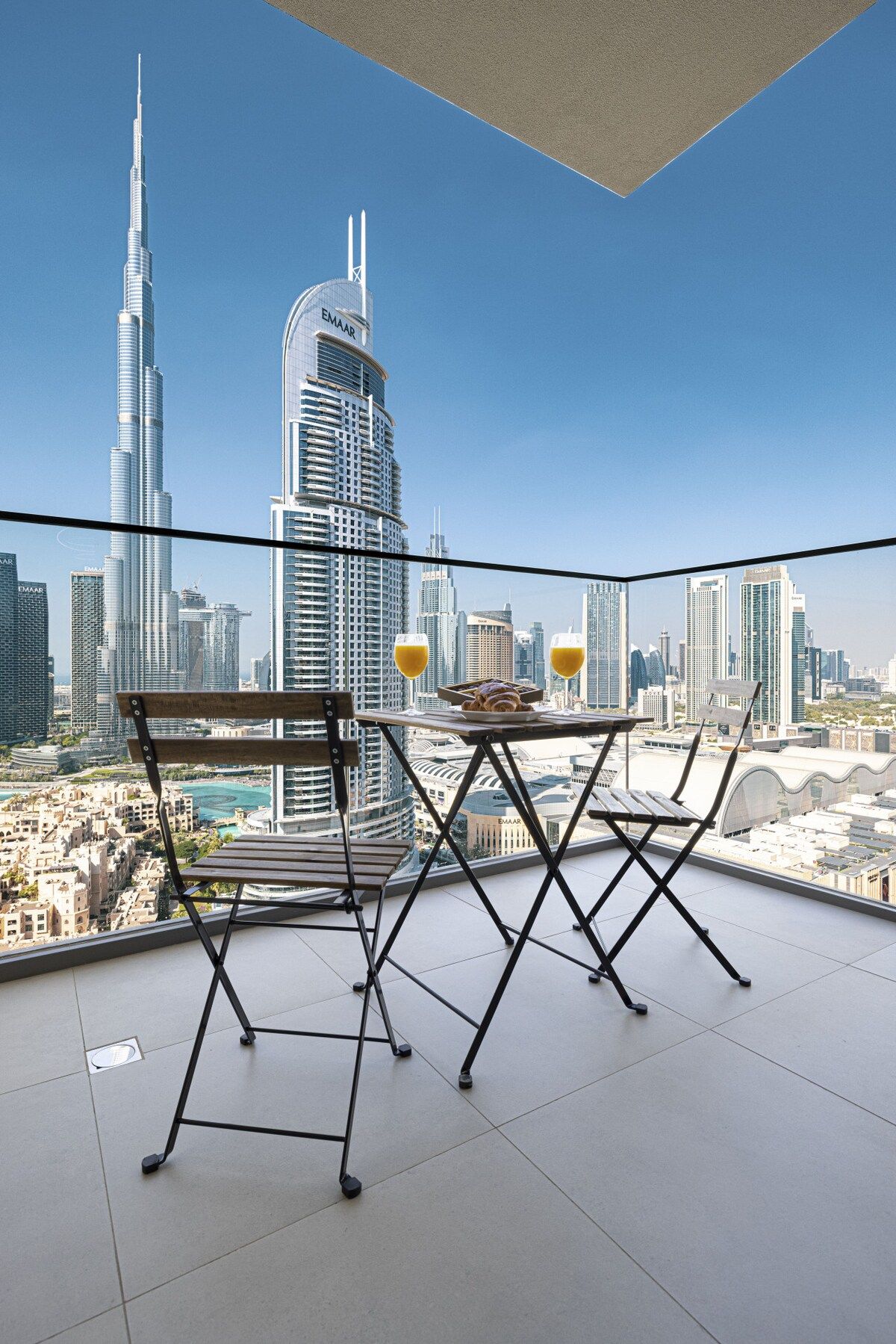 Un balcon avec vue sur la ville, comprenant une table et des chaises, ainsi que deux verres de jus d’orange.