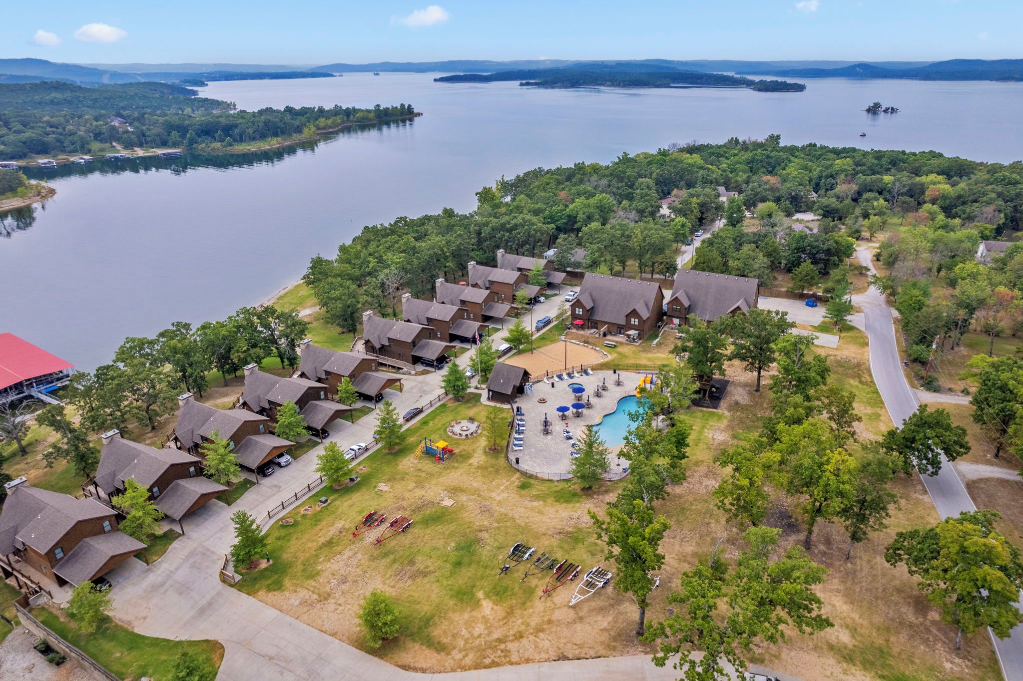 An aerial view of a lakeside resort with multiple cabins, a swimming pool, and a dock.