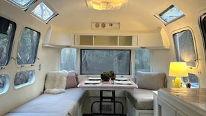 Ein kompaktes Wohnmobil-Interieur mit Küchenzeile, Essbereich und einer Sitzecke mit Fenstern.