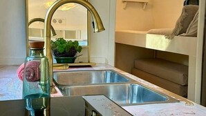 Eine kompakte Küche mit modernem Design, inklusive eines großen Spiegels, eines goldfarbenen Wasserhahns und einer integrierten Spüle.