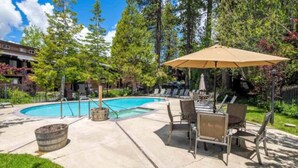 A pool area with lounge chairs and an umbrella, surrounded by trees and a building in the background.