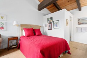 Ein Schlafzimmer mit einem großen Bett, Holzbalken an der Decke und gerahmten Bildern an der Wand.