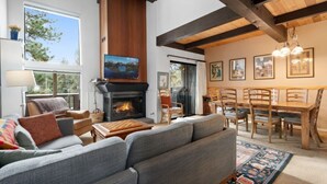 A cozy living room with a fireplace, comfortable seating, a dining area, and artwork on the walls.