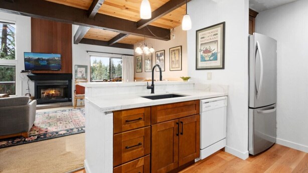 A modern kitchen with wooden beams, a built-in island with a sink, a stainless steel refrigerator, and a fireplace.