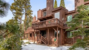 A wooden cabin with a balcony, surrounded by tall pine trees and snow on the ground.