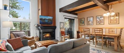 A cozy living room with a fireplace, comfortable seating, a dining area, and artwork on the walls.