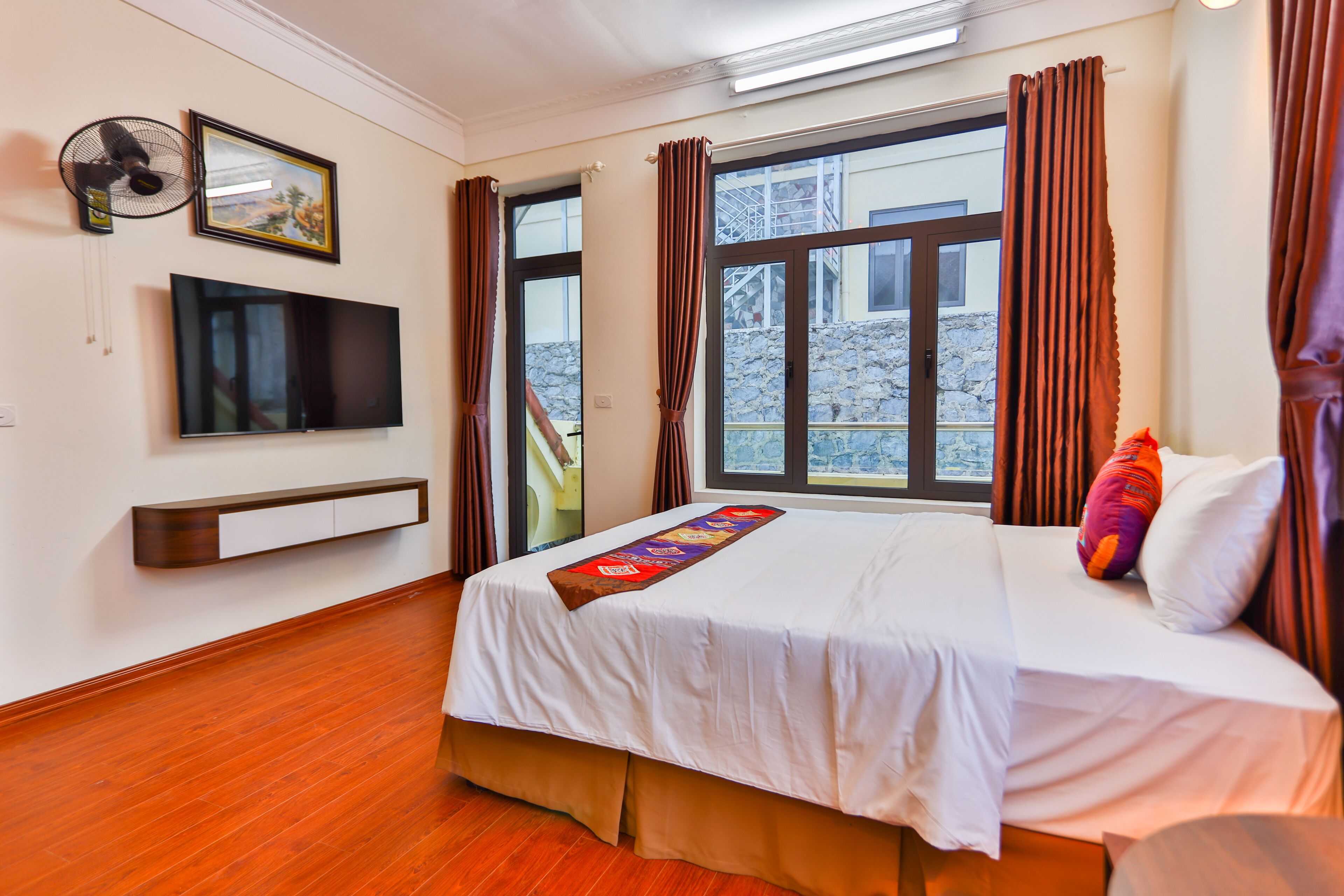 A hotel room with a bed, a TV, a window with curtains, and a view of the outside.