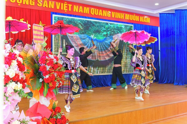 A stage with performers in traditional attire, a large screen in the background, and a banner with text. - JOVILLE HOTEL SAPA (Sa Pa)