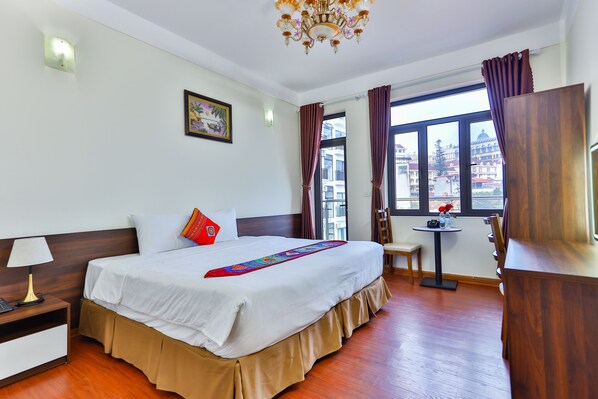 A hotel room with a large bed, a small table, a chair, a desk, and a window with curtains. - JOVILLE HOTEL SAPA (Sa Pa)