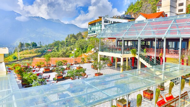 Un hotel con terraza de techo de cristal, zona de estar al aire libre y montañas al fondo.