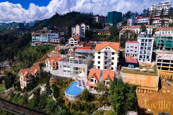 Un hotel amb piscina, envoltat de vegetació i diversos edificis.