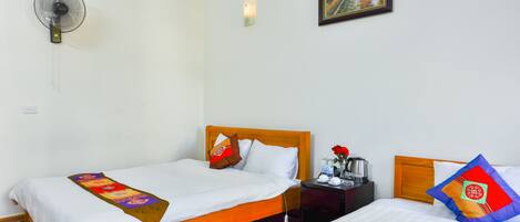 A hotel room with two beds, a nightstand with a lamp, a wall-mounted fan, and a painting on the wall.