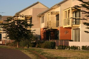 Un edificio residencial moderno con techo plano, ventanas grandes y un balcón con baranda metálica.
