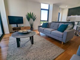 Una sala de estar moderna con un sofá gris, una mesa redonda de centro, un televisor de pantalla plana y un ventanal grande.