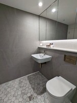 Un baño moderno con lavamanos, inodoro y zona de ducha blancos.