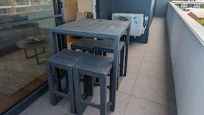 A balcony with a table and chairs, a sliding glass door, and a view of the cityscape. - Newcastle Interchange Apartments (Wickham)