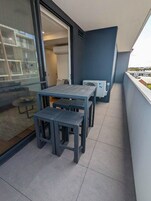 Un balcón con mesa y sillas, un ventanal corredero y vistas de la ciudad.