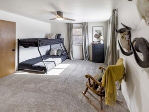 A room with bunk beds, a ceiling fan, a dresser, a rocking chair, and a window with curtains.