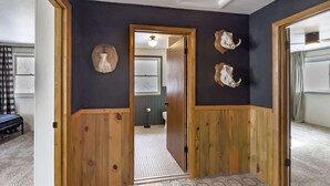 A hallway with wooden paneling, a patterned floor, and a door leading to a bathroom with a toilet and sink. - Mountain Meadow Retreat near Park City (Peoa)