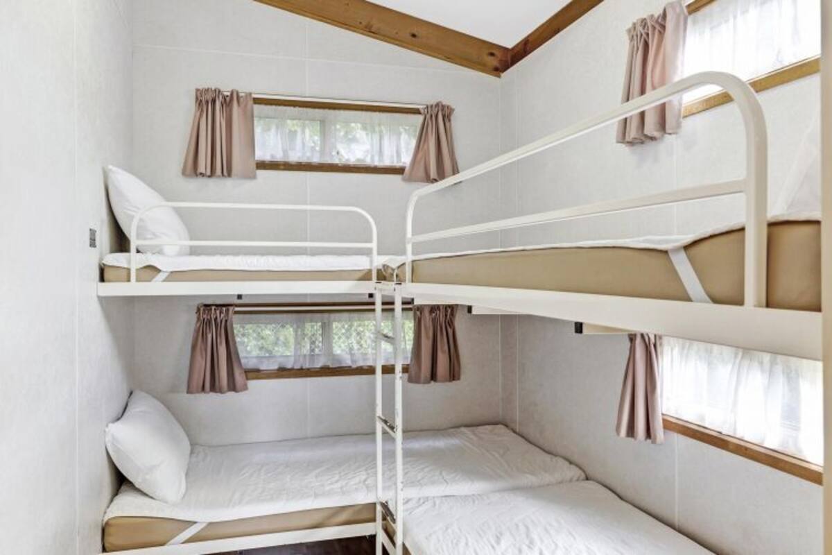 Dormitorio con literas, cortinas, una ventana y techo de madera.