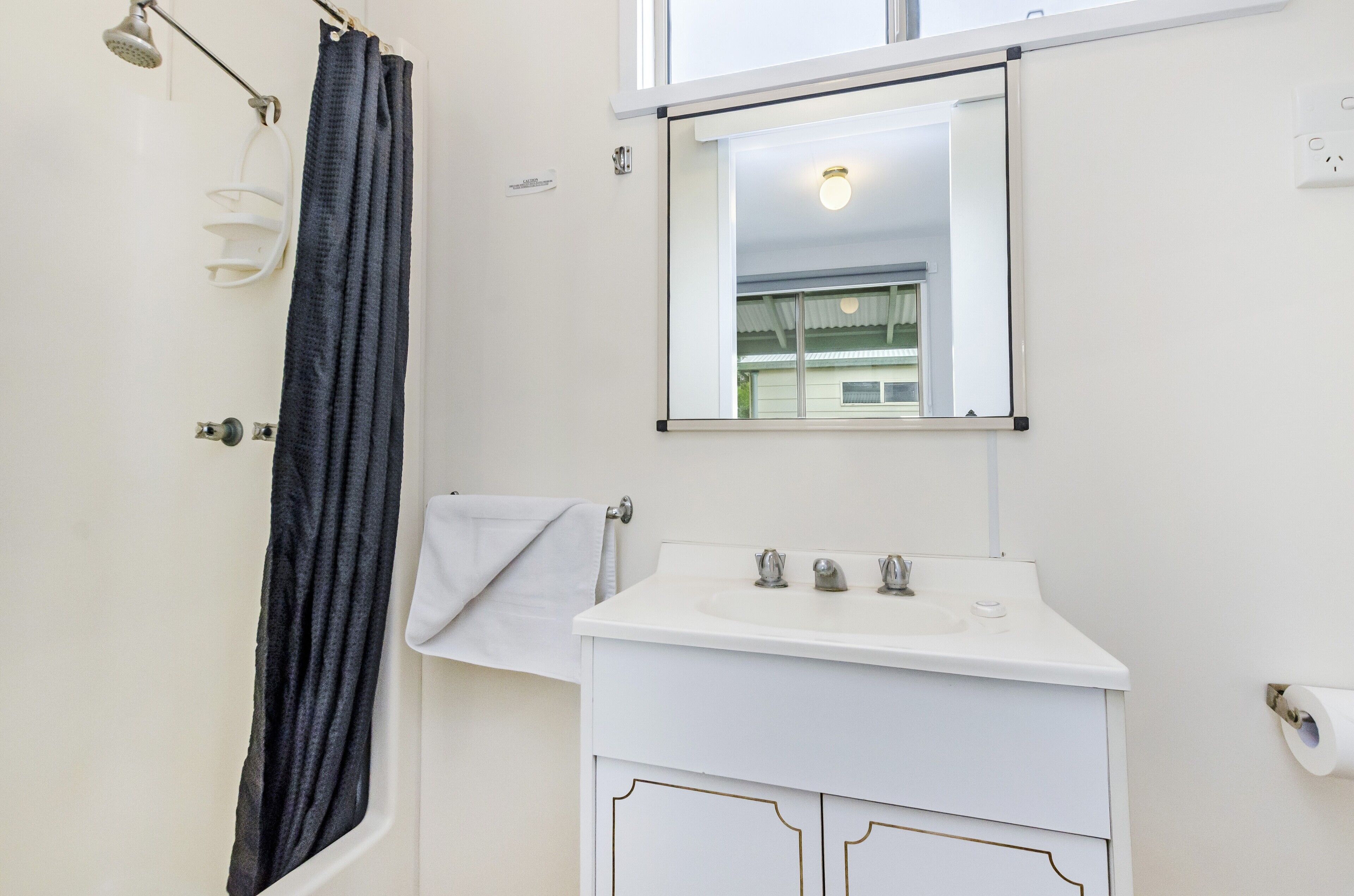 Ein Badezimmer mit einem weißen Waschbecken, einem Spiegel, einer Duschkabine mit Vorhang und einem Handtuch an der Wand.
