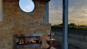 Una chimenea de piedra con puerta de cristal, un ventanal redondo encima y vistas a un viñedo al fondo.