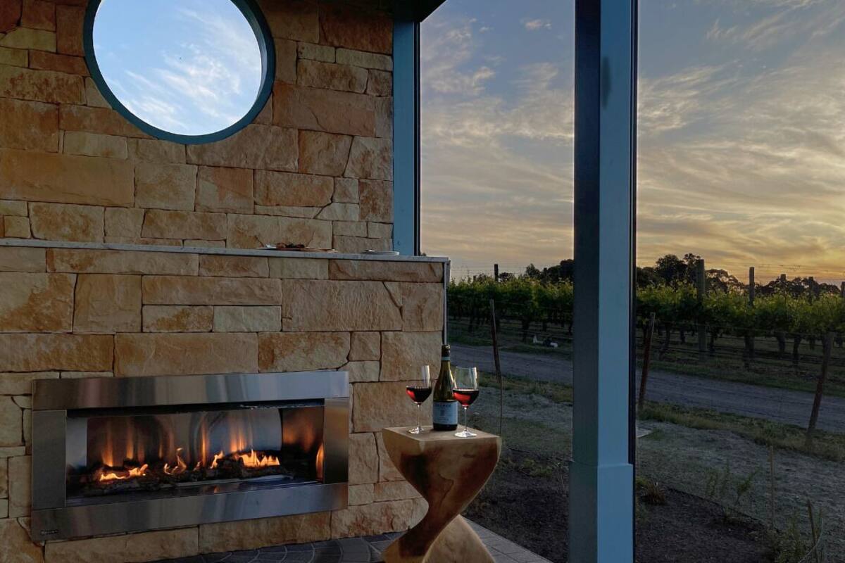 A stone fireplace with a glass door, a round window above it, and a view of a vineyard in the background.