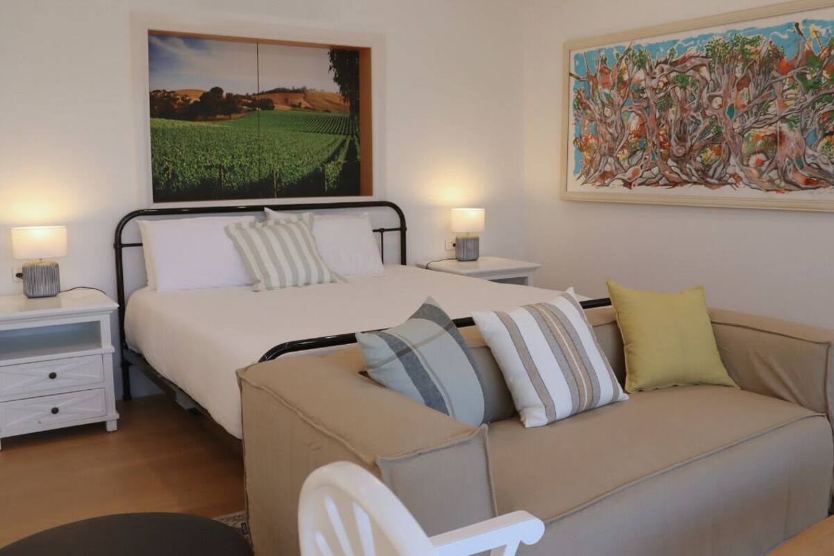 A bedroom with a bed, a sofa, two bedside tables, and two wall-mounted lamps.