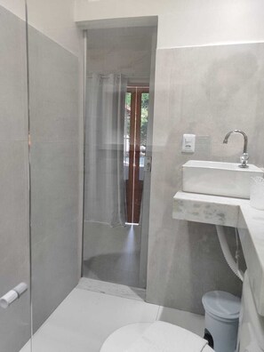 A bathroom with a glass shower enclosure, a white sink, and a visible trash bin.