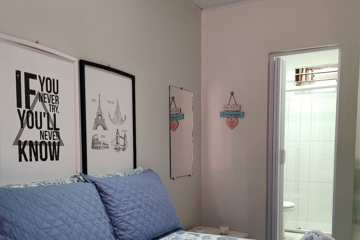 Une chambre à coucher avec un lit, des oreillers bleus, une citation encadrée accrochée au mur et une porte donnant sur une salle de bain.