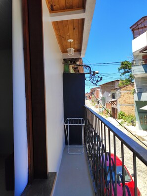 A balcony with a metal drying rack, a wooden ceiling, and a view of a red car and buildings in the background.