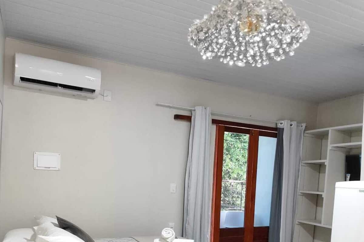 Une chambre d’hôtel avec un lit, une petite table sur laquelle est posé un vase de fleurs, un réfrigérateur et une fenêtre avec des rideaux.