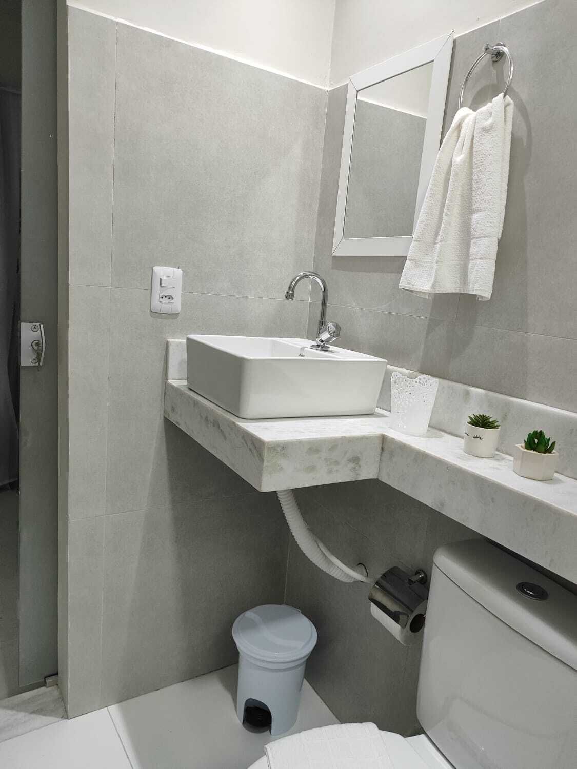 A modern bathroom with a white sink, a mirror, a towel rack, and a small potted plant.