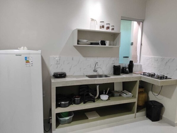 A compact kitchen with a refrigerator, a sink, a stove, and a countertop with various kitchen items. - Casa de Mel (Itacaré)