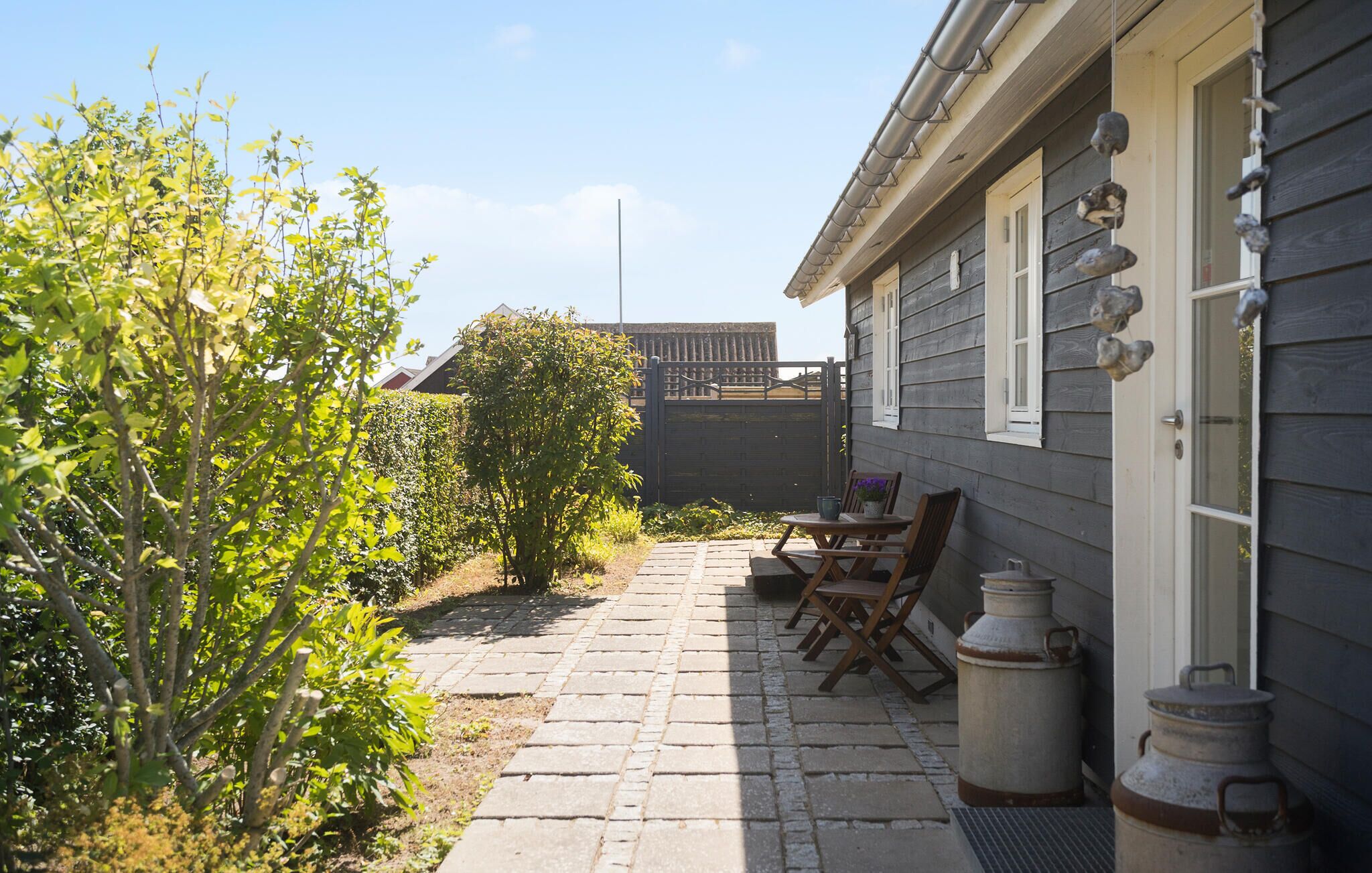 Un patio con mesa y sillas, un pequeño jardín y una casa con revestimiento exterior oscuro.