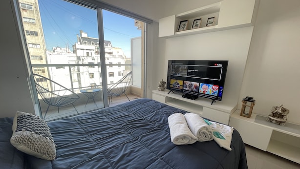 A modern bedroom with a large bed, a TV, and a balcony with a chair. - San Telmo Oasis Contemporary Luxurious Studios Num6863 (Buenos Aires)