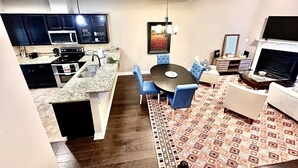 Een modern appartement met een keuken, eethoek en woonkamer. Het heeft een eettafel met stoelen, een bank, een televisie en een open haard.