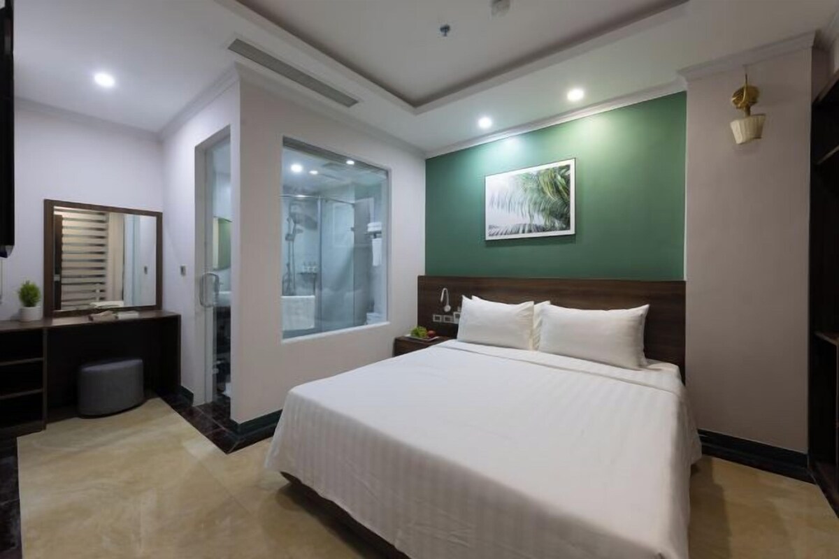 A hotel room with a large bed, a bedside table, a mirror, a window, and a green accent wall.